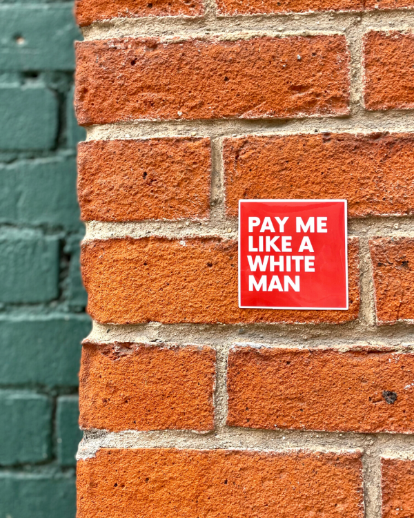 Red sticker that says "pay me like a white man" on a red brick wall