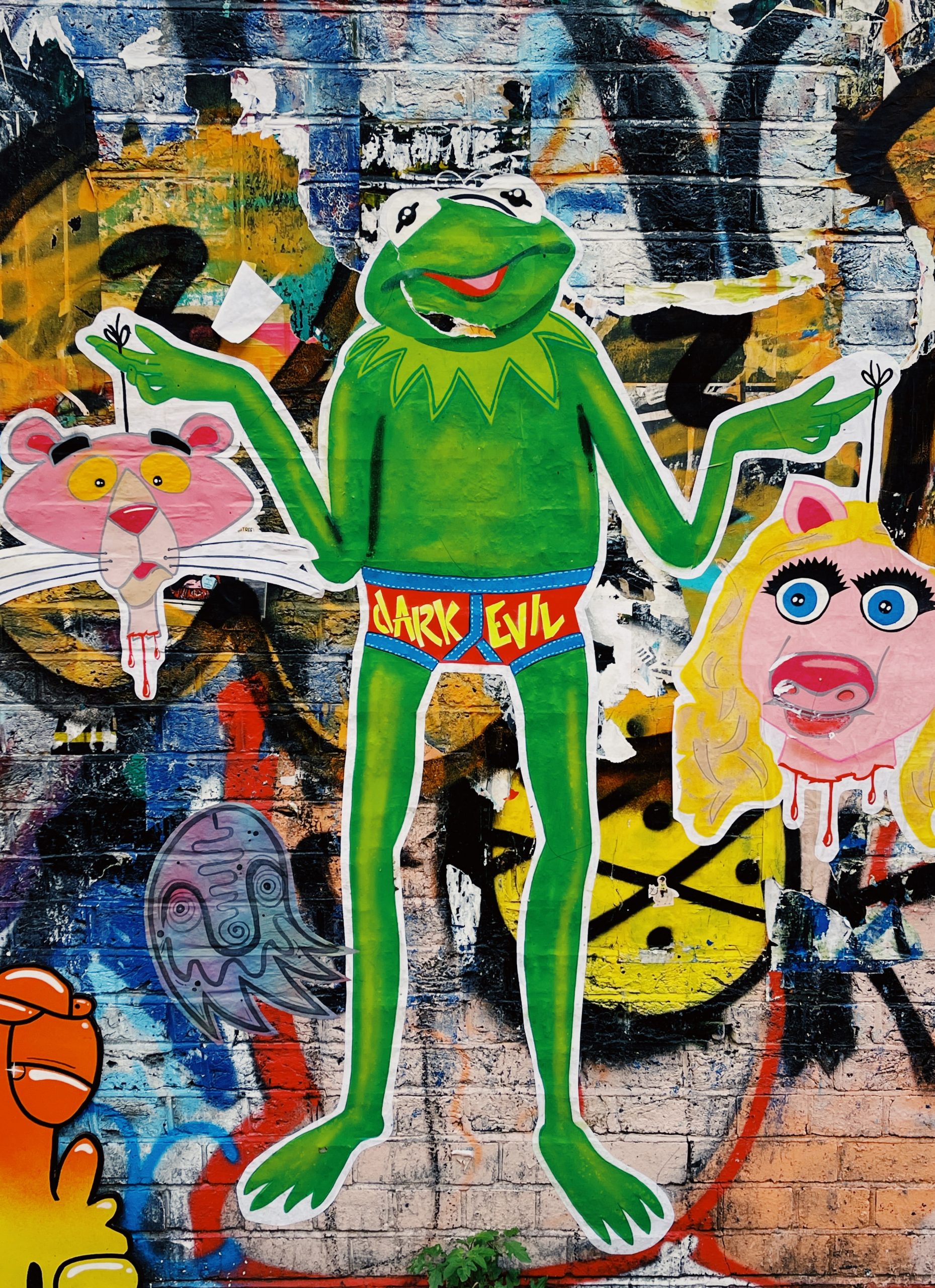 Street art mural of Kermit of the frog shrugging and wearing underwear that reads "Dark Evil", with a backdrop of other cartoon characters including Ms. Piggy  