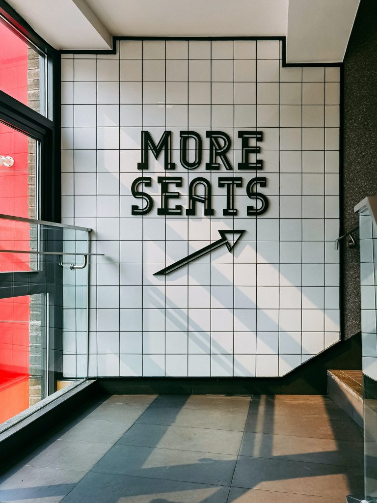 White wall with black more seats sign and arrow pointing up stairs