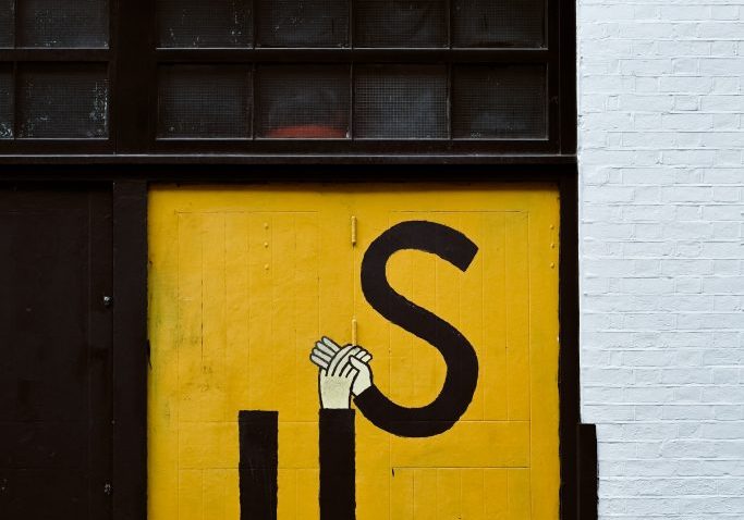 Graffiti of two hands holding one in the shape of the letter u and the other in the shape of the letter s